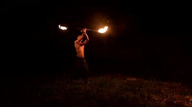 Düşük anahtar. Uzun saçlı ve çıplak gövde ile genç erkek siyah bir gece video yavaş hareket açık havada yanan meşale döner. Modern fakir bir yanan personel ile hileler yapar