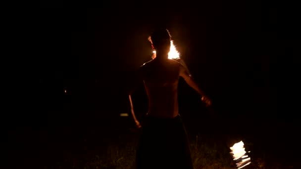 Très discret. Jeune homme aux cheveux longs et au torse nu tourne torche brûlante à l'extérieur sur une vidéo de nuit noire au ralenti. Fakir moderne fait des tours avec un bâton brûlant 