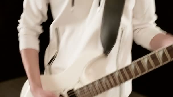 Close-up Guitarrista de ritmo elegante com diferentes olhos em roupas brancas em um fundo preto tocando expressivamente a guitarra branca em um estúdio preto — Vídeo de Stock