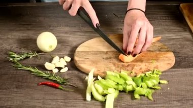 Kadın şef ellerinin, dilimlenmiş sebzelerin yanındaki tahta kesme tahtasına soyulmuş havuçları dilimlemesinin yakın çekimi. Vejetaryenlik kavramı