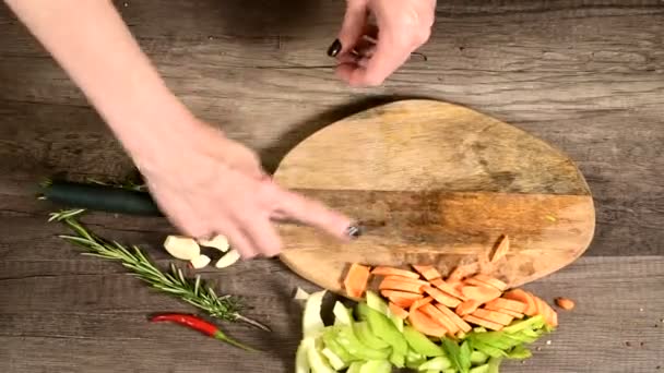 Primer plano de las manos del chef rebanando zanahorias peladas en una tabla de cortar de madera junto a las verduras en rodajas. El concepto de vegetarianismo — Vídeos de Stock