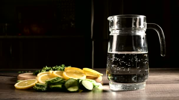 Sliced lemon cucumbers and mint leaves on a wooden cutting board next to a glass carafe with sparkling water — Stock Video