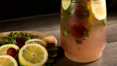 Bir cam carafe yakın çekim limon ve salatalık dilimleri nane ve dondurulmuş çilek köpüklü suda karıştırılır vardır. Limonata Cam Dönüşümlü Meyveler