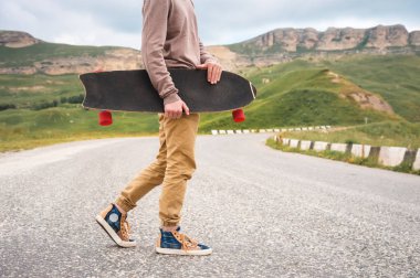 Şık bir genç adam gün batımından sonra akşam elinde bir paten veya longboard ile dolambaçlı bir dağ yolu boyunca yürüyor. Gençlik spor ve seyahat hobileri kavramı