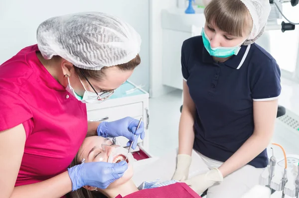 No consultório dos dentistas. Exame da cavidade oral de uma jovem paciente por um médico e assistente. Prevenção do tratamento dentário e cárie. Conceito de higiene oral — Fotografia de Stock