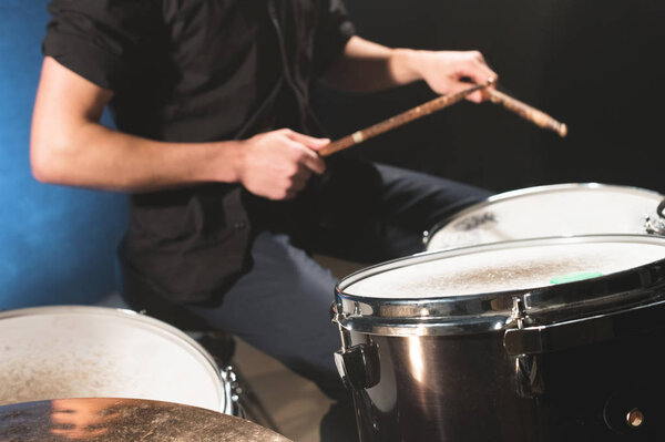 Close-up of a male drummers hand holding drum sticks while sitting behind a drum set