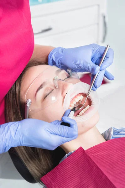 Κοντινό πλαίσιο ενός οδοντιάτρου που εφαρμόζει πολυμερές από μια σύριγγα στο εσωτερικό ενός νεαρού ασθενούς μπροστινό δόντι σε ένα οδοντιατρείο — Φωτογραφία Αρχείου