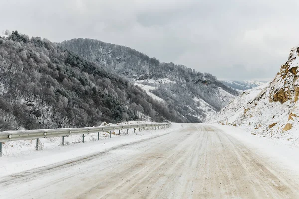 Пустая горная асфальтовая дорога зимой покрыта снегом в облачный день. Концепция вождения автомобиля в зимний лед и путешествия — стоковое фото