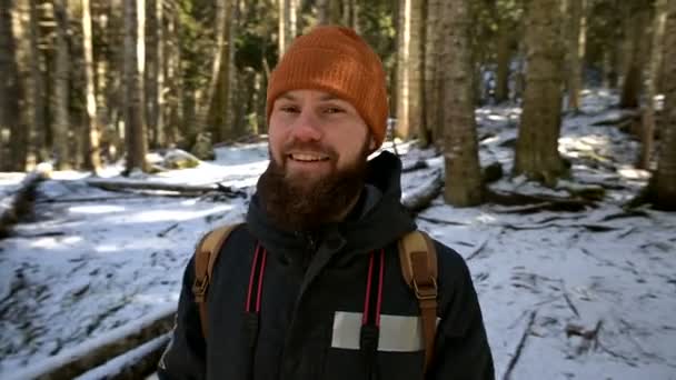 Retrato de un alegre joven barbudo riendo con una mochila en un bosque invernal de coníferas — Vídeo de stock