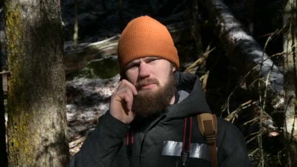 Un barbudo con sombrero hablando por celular en un bosque de coníferas. El concepto de comunicación celular en lugares de difícil acceso — Vídeos de Stock
