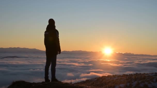 La silhouette di un uomo si erge al tramonto sopra le nuvole e contempla il sole che tramonta. Il concetto di tranquillità e piacere nel viaggiare — Video Stock