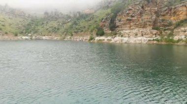 Kayalık bir sahilin havadan görünümü. Bulutlu hava ve sis tepeler arasında Dağ turkuaz göl. Kuzey Kafkasya Manzaraları