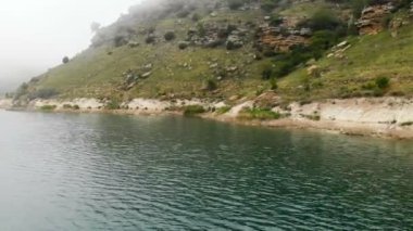 Kayalık bir sahilin havadan görünümü. Bulutlu hava ve sis tepeler arasında Dağ turkuaz göl. Kuzey Kafkasya Manzaraları