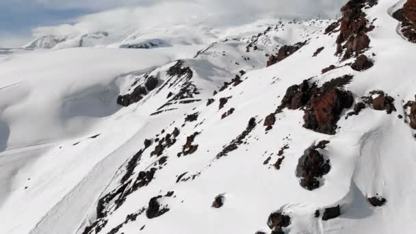 Widok z lotu ptaka na zimowy krajobraz górski. Pokryte śniegiem skaliste zbocza kurortu południowego regionu Elbrus z trasami narciarskimi na śniegu. Koncepcja sportów zimowych — Wideo stockowe