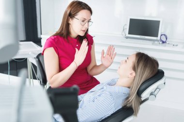 Dişçi kadın doktor bir tıbbi ofiste dişçi sandalyede oturan genç bir hasta konuşuyor. Müşteri ve dış görsel muayene ile ilk konuşma