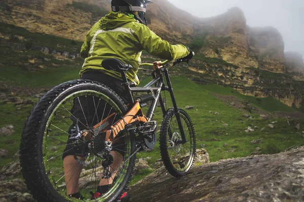 Vista trasera gran angular de un hombre en una bicicleta de montaña se encuentra en un terreno rocoso y mira a una roca. El concepto de una bicicleta de montaña y mtb cuesta abajo —  Fotos de Stock