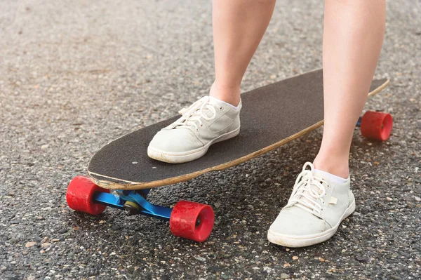 Közeli fel a női lábak rongyos cipők egy Longboard a háttérben aszfalt naplementekor. Nagy gördeszka a lány lába. Ifjúsági szabadidőkoncepció — Stock Fotó