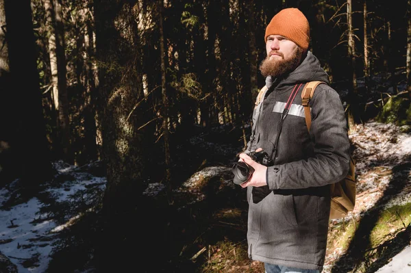 Портрет бородатого фотографа з рефлекторною камерою в руках в зимовому хвойному лісі. Концепція подорожей фотографіями — стокове фото