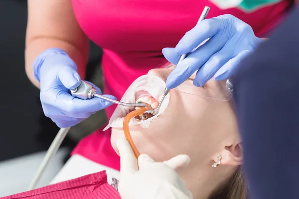 Στο οδοντιατρείο. Κοντινό-up εξέταση της στοματικής κοιλότητας μιας νεαρής γυναικείας ασθενούς από γιατρό και βοηθό. Πρόληψη της οδοντιατρικής θεραπείας και της τερηδόνας. Έννοια της στοματικής υγιεινής — Φωτογραφία Αρχείου