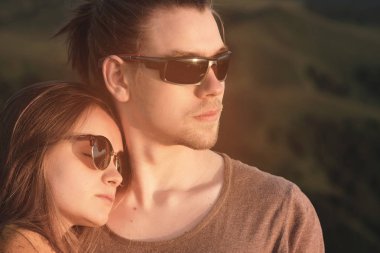 Yakın çekim Romantik bir genç hipster çift sarılma Portresi. Onlar bir dağ yeşil vadi ve bulutlar fon karşı dağların yüksek doğada bir kucaklama standı.