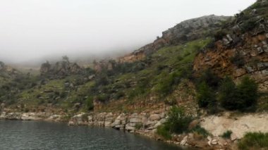 Kayalık bir sahilin havadan görünümü. Bulutlu hava ve sis tepeler arasında Dağ turkuaz göl. Kuzey Kafkasya Manzaraları