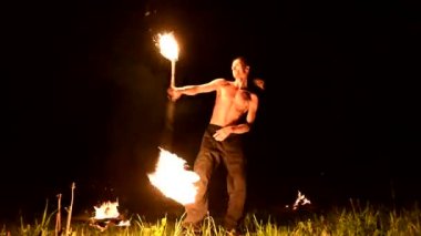 Düşük anahtar. Uzun saçlı ve çıplak gövde ile genç erkek siyah bir gece video yavaş hareket açık havada yanan meşale döner. Modern fakir bir yanan personel ile hileler yapar