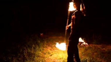 Düşük anahtar. Uzun saçlı ve çıplak gövde ile genç erkek siyah bir gece video yavaş hareket açık havada yanan meşale döner. Modern fakir bir yanan personel ile hileler yapar