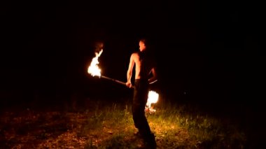 Düşük anahtar. Uzun saçlı ve çıplak gövde ile genç erkek siyah bir gece video yavaş hareket açık havada yanan meşale döner. Modern fakir bir yanan personel ile hileler yapar