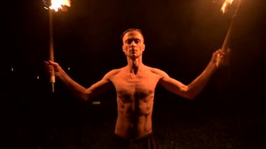 Close. Düşük anahtar. Uzun saçlı ve çıplak gövde ile genç erkek siyah bir gece video yavaş hareket açık havada yanan meşale döner. Modern fakir bir yanan personel ile hileler yapar