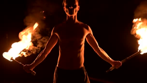 Close-up. Low key. Young male with long hair and bare torso rotates burning torch outdoors on a black night video slow motion. Modern fakir does tricks with a burning staff — Stock Video