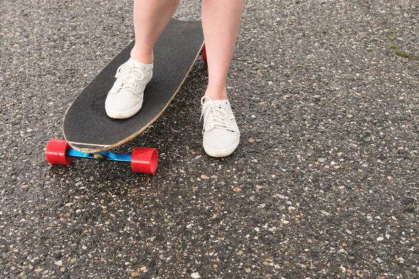 Közeli fel a női lábak rongyos cipők egy Longboard a háttérben aszfalt naplementekor. Nagy gördeszka a lány lába. Ifjúsági szabadidőkoncepció — Stock Fotó