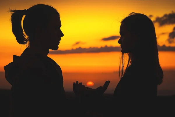 Närbild av silhuetter av en ung Millenial par i kärlek händer håller solen med en man och flicka mot solnedgången Golden Sky. De tittar på varandra. Unga familjen — Stockfoto