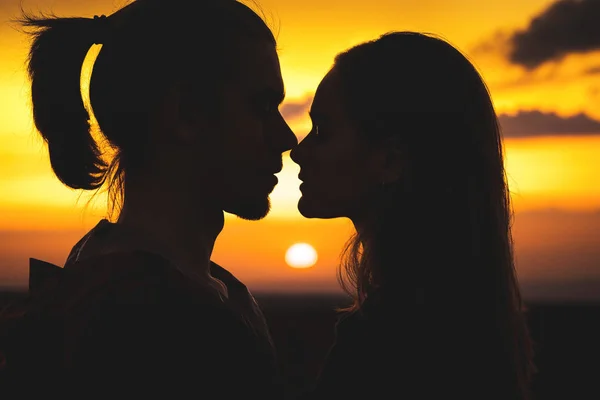 Primer plano de las siluetas de una joven pareja milenaria enamorada preparándose para besarse con un hombre y una niña contra el cielo dorado atardecer. Se miran unos a otros. Familia joven — Foto de Stock