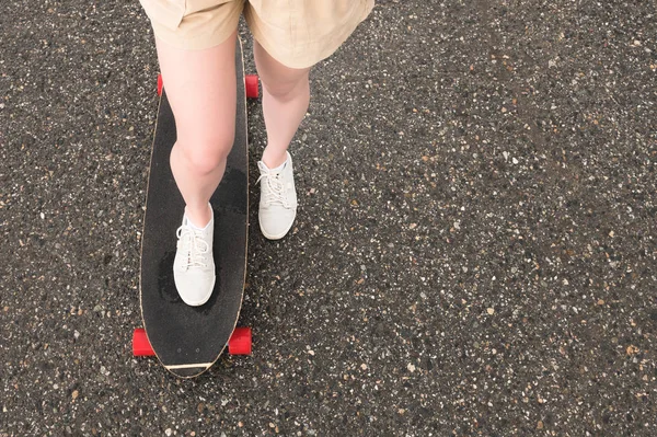 Close-up dari kaki perempuan dalam sepatu olahraga kain pada longboard di latar aspal saat matahari terbenam. skateboard besar dengan kaki perempuan. Konsep liburan anak muda — Stok Foto