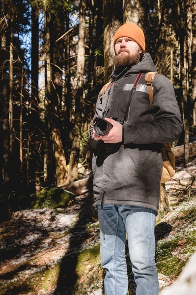 Portrét vousatého fotografa s reflexní kamerou v dlaních v zimě jehličnatých lesů. Koncepce cestování fotografií — Stock fotografie