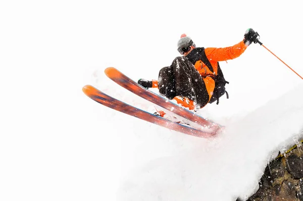 Ο αθλητής σκιέρ σε ένα φωτεινό φόντο με ένα άλμα μετακινείται από την οροφή ενός χιονισμένη καλύβα με ιπτάμενες νιφάδες χιονιού. Η έννοια των χειμερινών σπορ σκι — Φωτογραφία Αρχείου