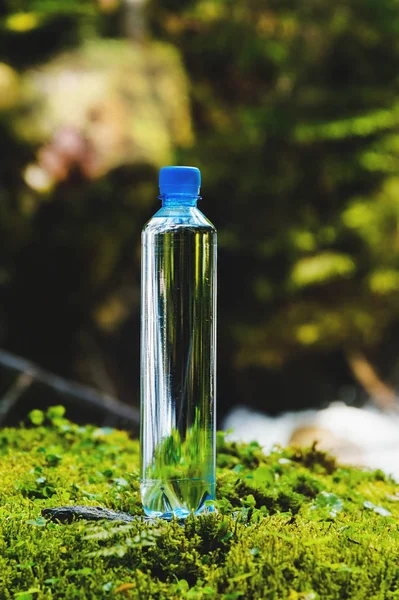 Plastic bottle blue cap with fresh drinking water on a background of green forest stands on a stone with moss. The concept of pure natural mountain water