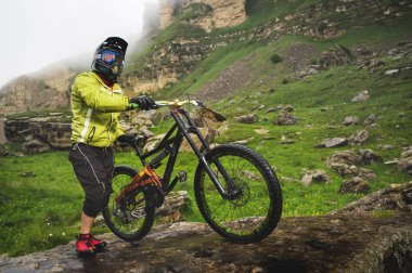 Dağ bisikletinde kayalık bir arazide duran ve kayaya bakan bir adamın yan görüntüsü. Bir dağ bisikleti ve mtb yokuş aşağı kavramı