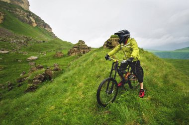 Dağ bisikletinde kayalık bir arazide duran ve kayaya bakan bir adamın yan görüntüsü. Bir dağ bisikleti ve mtb yokuş aşağı kavramı