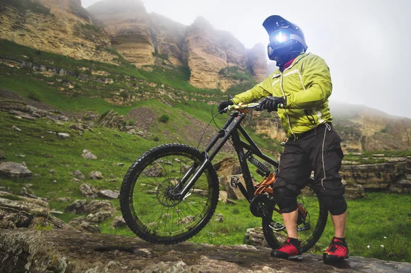 Vista laterale di un uomo in mountain bike in piedi su un terreno roccioso e guardando una roccia. Il concetto di mountain bike e mtb downhill — Foto Stock