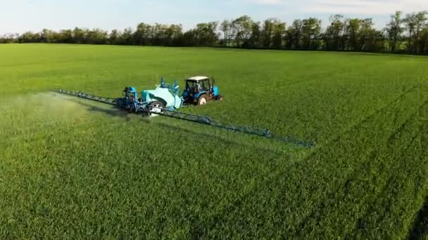 Luftaufnahme des Traktors, der das grüne Feld durch eine spezielle Installation bewässert. Prozess des Sprühens von Feldgehölzen mit Pestiziden und Schutz gegen Insekten von Nagetieren, Parasiten und Schädlingen. — Stockvideo