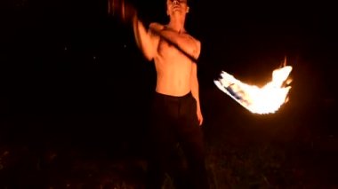 Düşük anahtar. Uzun saçlı ve çıplak gövde ile genç erkek siyah bir gece video yavaş hareket açık havada yanan meşale döner. Modern fakir bir yanan personel ile hileler yapar