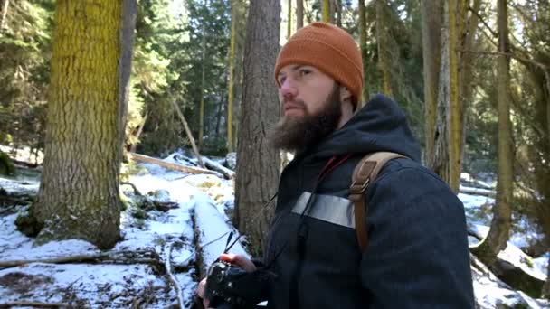 一个留着胡子的男性旅行者摄影师带着相机在冬天的森林里拍摄大自然的照片。博客和摄影艺术家的旅行概念 — 图库视频影像