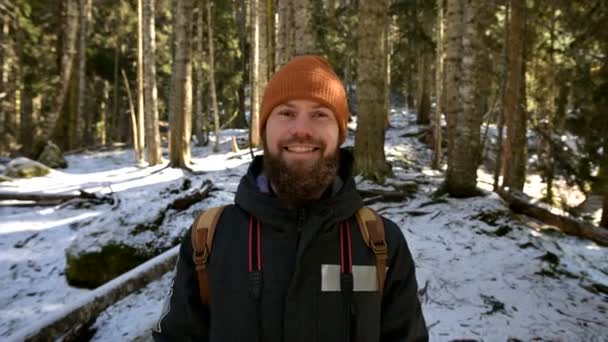 Retrato de un alegre joven barbudo riendo con una mochila en un bosque invernal de coníferas — Vídeo de stock
