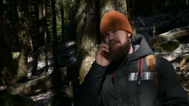 Een bebaarde man in een hoed praten op een mobiele telefoon in een naald bos. Het concept van mobiele communicatie op moeilijk bereikbare plaatsen — Stockvideo