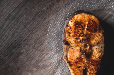 Close-up one grilled cum salmon keta fish steak on a glass transparent plate on a dark wood table background. A little overdone dish. Sea food for lovers of fried