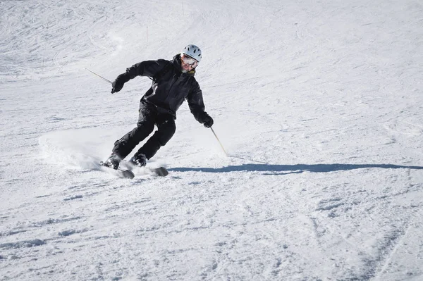 Brodaty dojrzały w wieku mężczyzna narciarz w czarnym garnitur narciarski schodzi wzdłuż ośnieżone stoku ośrodka narciarskiego. Koncepcja sportu w dorosłości — Zdjęcie stockowe