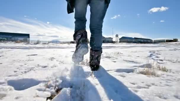 Слідом за чоловічими ногами в джинсах і теплим взуттям, що йдуть снігом в зимовий сонячний день. Крупним планом низький кут. Вид ззаду — стокове відео