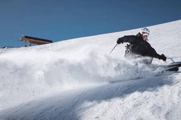 Un esquiador de edad madura barbudo con un traje de esquí negro desciende por la ladera nevada de una estación de esquí. Sedación en la pendiente y polvo de nieve. El concepto de deporte en la edad adulta — Foto de Stock