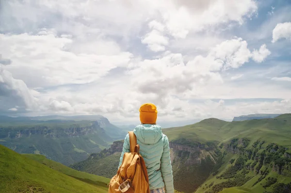 A kilátás a hátán egy turista lány egy hátizsák áll, és nézi a hegyi zöld völgyek és fennsík egy napsütéses napon az ég és a felhők. Utazási és idegenforgalmi koncepció — Stock Fotó